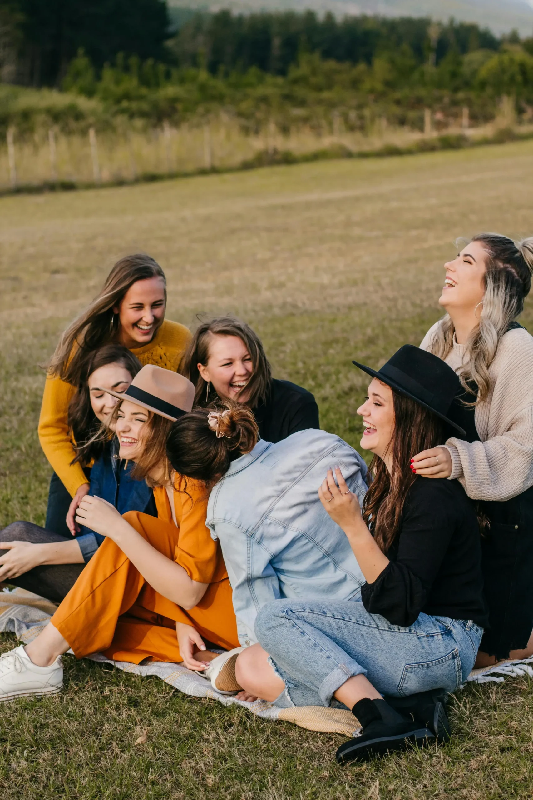 A group of eight women sitting together on grass, laughing and enjoying each other's company in a candid moment